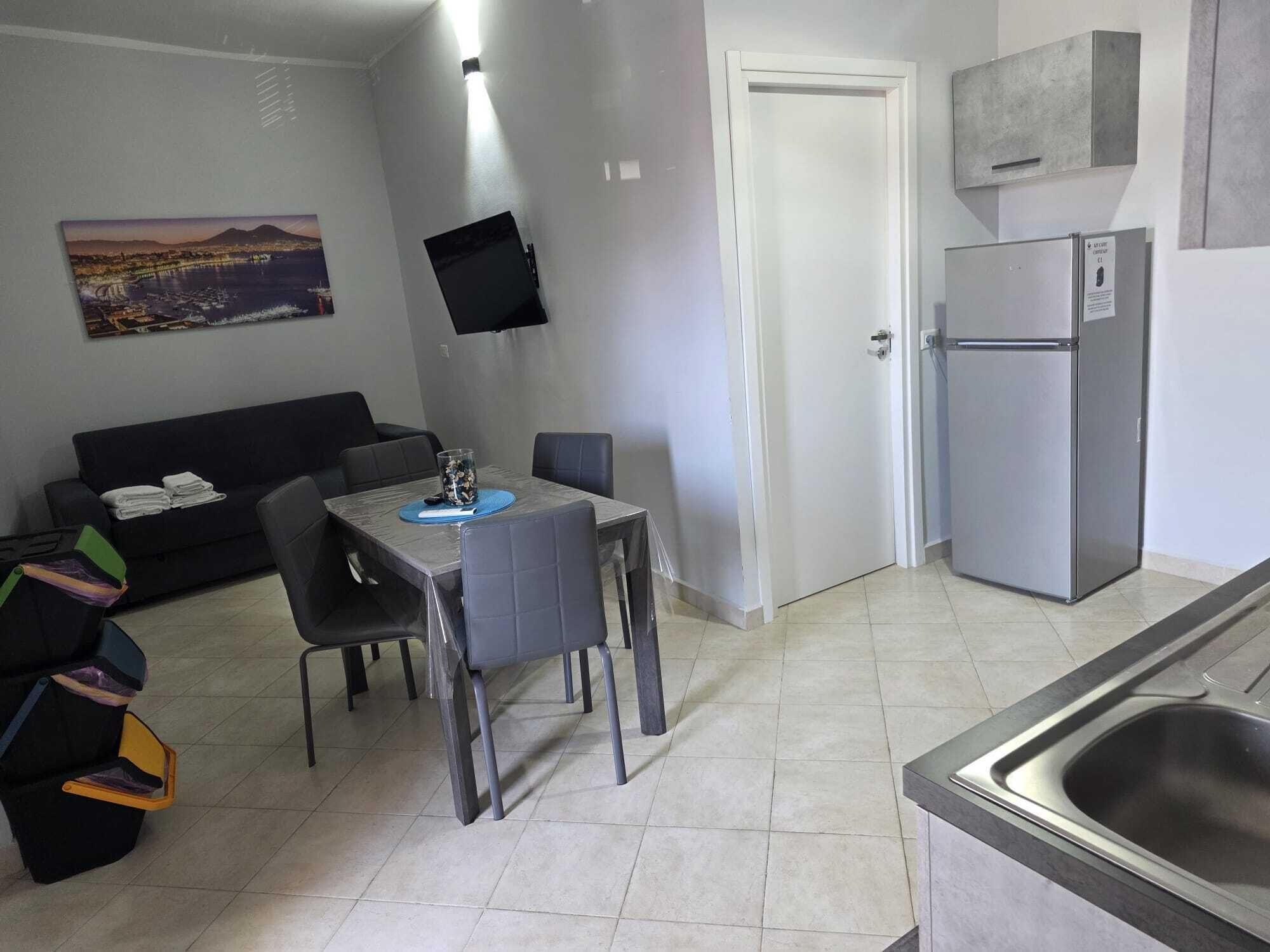 A compact kitchen with a dining table, chairs, a refrigerator, and a flat-screen TV mounted on the wall.