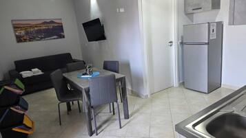 A compact kitchen with a dining table, chairs, a refrigerator, and a flat-screen TV mounted on the wall.