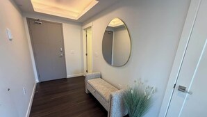 Un pasillo con piso de madera oscura, un banco, un espejo redondo y una planta en maceta.