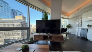 Una sala de estar moderna con un televisor de pantalla plana grande, muebles de madera y vistas de la ciudad a través de amplios ventanales.