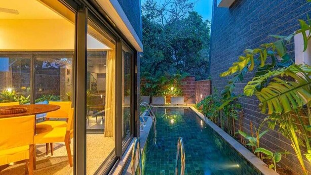 A modern outdoor pool area with a glass-enclosed patio and a brick wall. - Cozy Nest 4Bhk Private Villa with Private Pool, Anjuna Beach North Goa (Vagator)