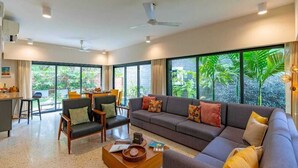 A spacious living room with a sofa, chairs, a coffee table, and large windows offering a view of greenery. - Cozy Nest 4Bhk Private Villa with Private Pool, Anjuna Beach North Goa (Vagator)