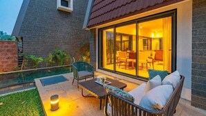 A modern outdoor patio with a glass door leading to a dining area, a pool, and a well-maintained garden. - Cozy Nest 4Bhk Private Villa with Private Pool, Anjuna Beach North Goa (Vagator)