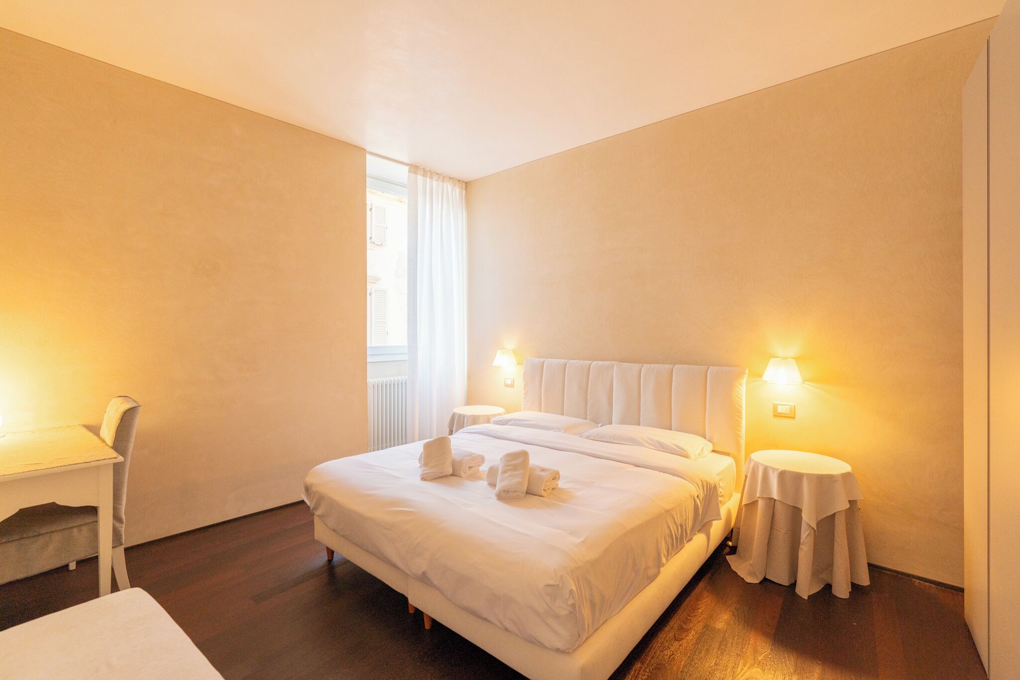 A hotel room with a large bed, two bedside tables, a chair, and a window with curtains.