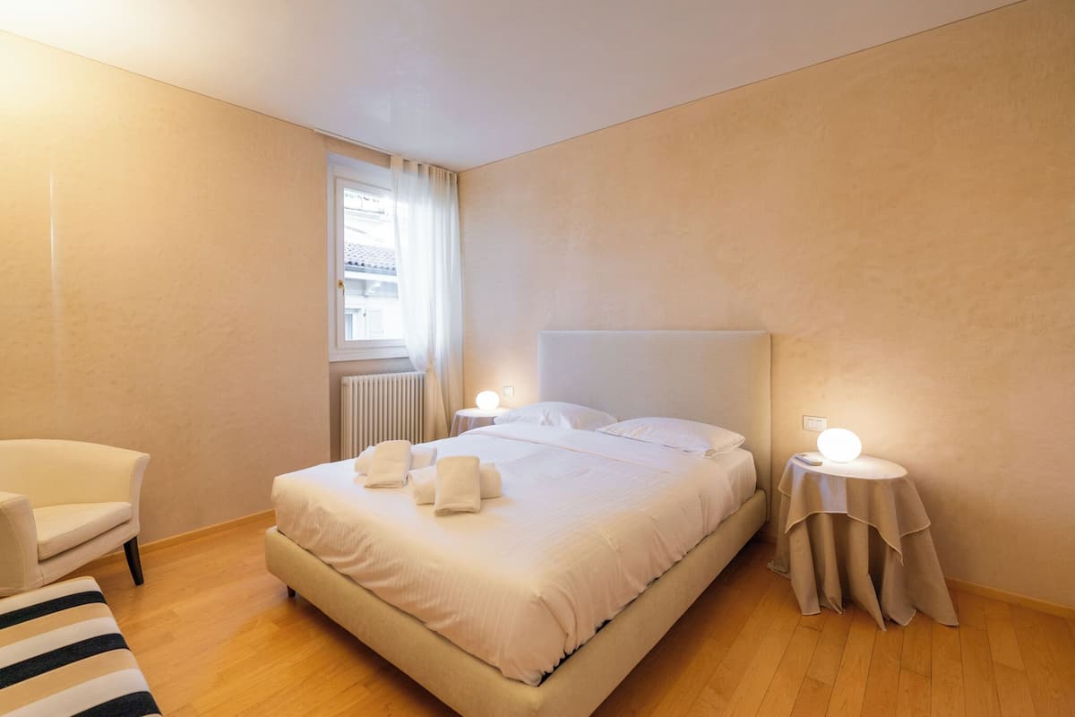 A neatly arranged bedroom with a large bed, bedside tables, a chair, and a window with curtains.