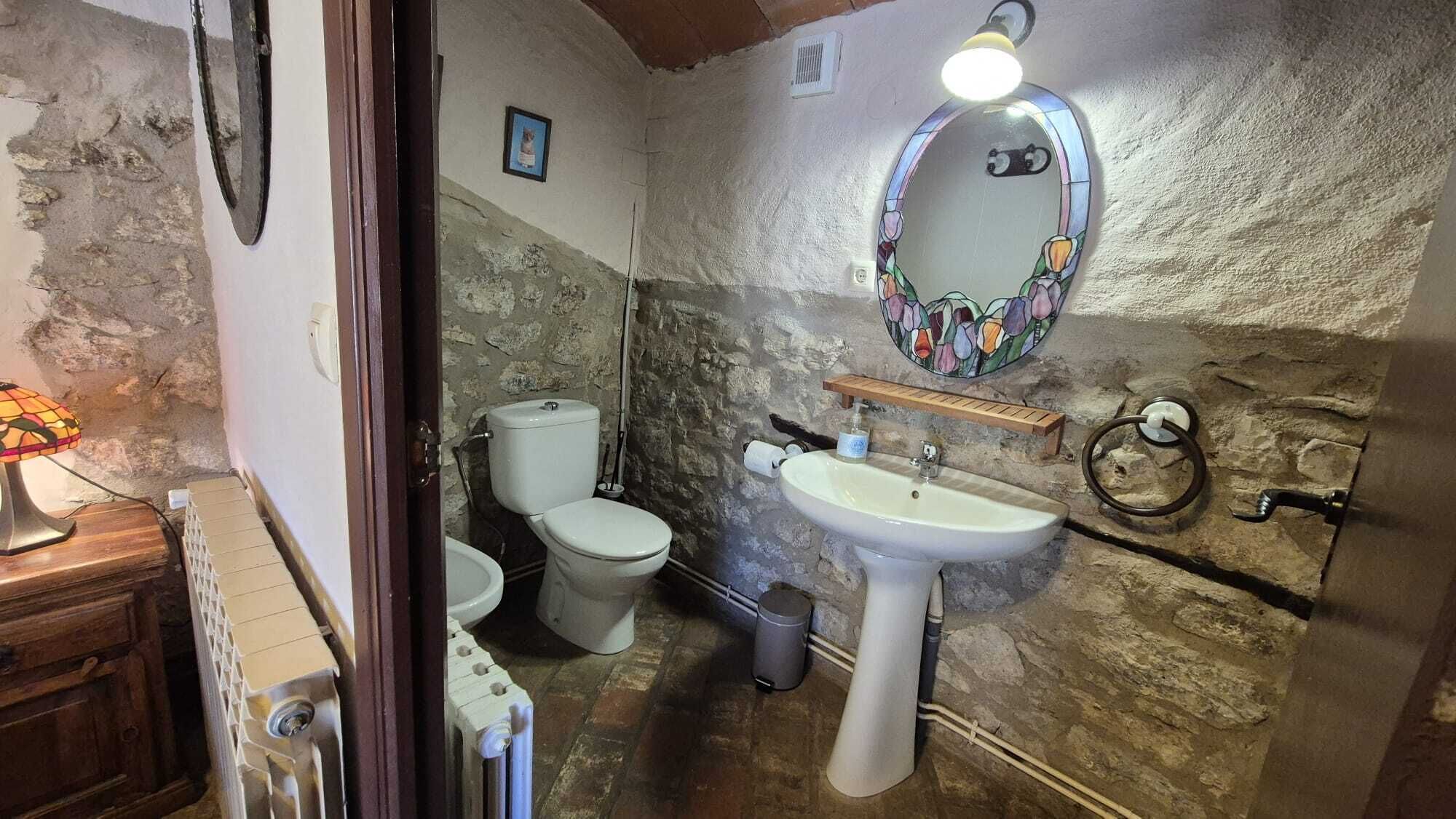A bathroom with a stone wall, a white sink, a toilet, and a wooden cabinet.