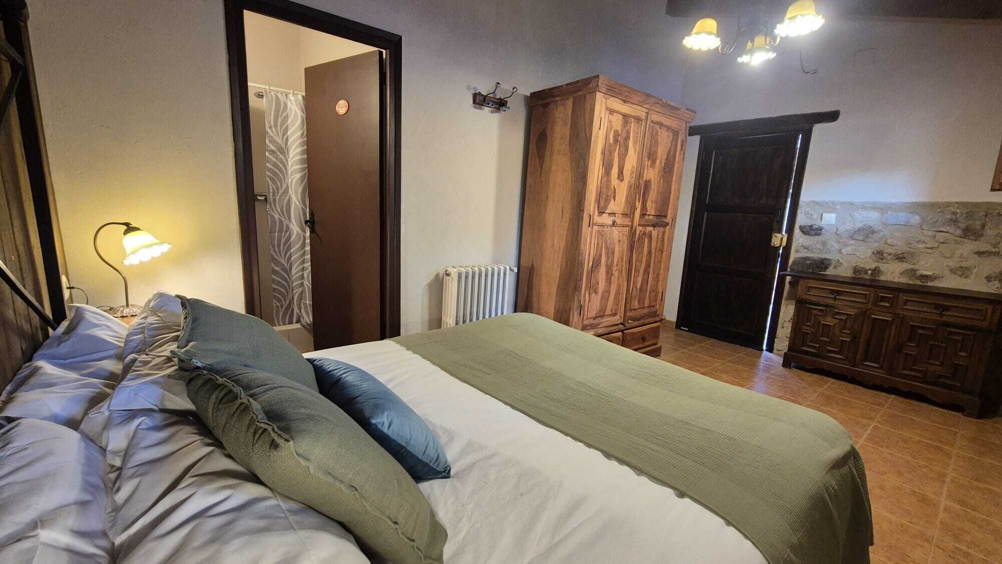 A bedroom with a bed, a wooden wardrobe, a radiator, and a bathroom door.