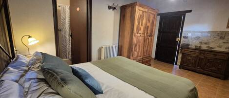 Quarto com cama, guarda-roupa de madeira, radiador e porta de banheiro.
