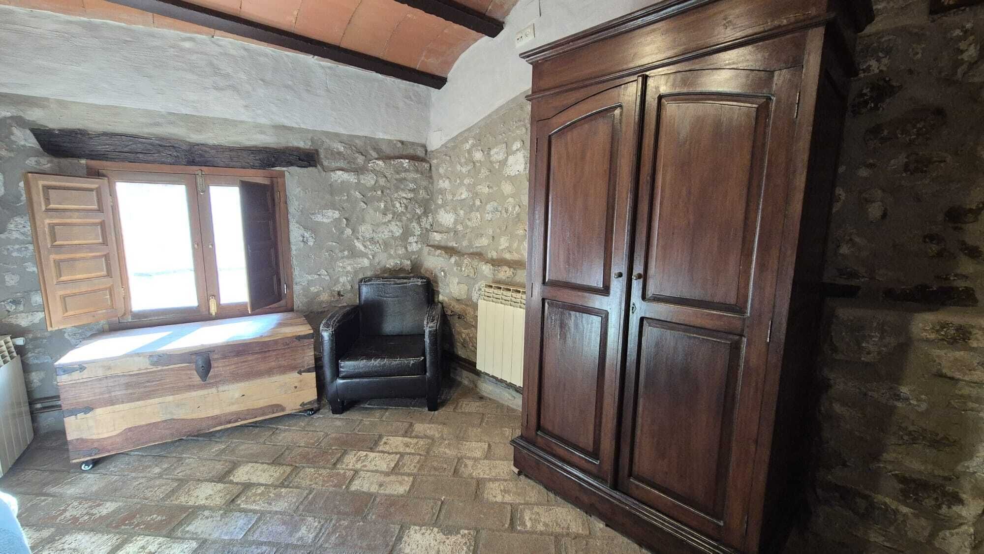 Habitació rústica amb paret de pedra, un armari de fusta, una banca i un radiador.