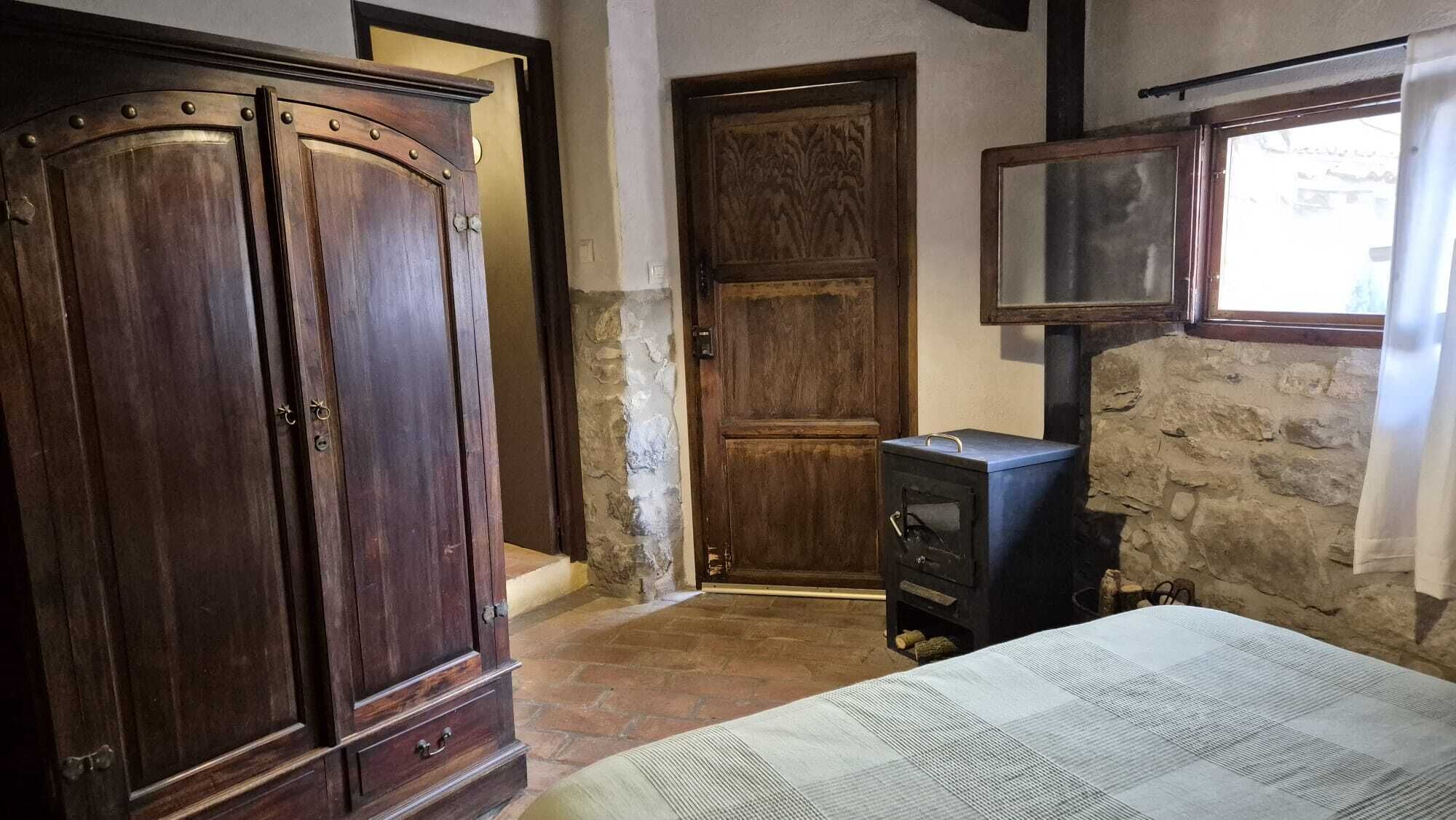 Un dormitorio con un armario grande de madera, una pared de piedra y una cama con manta a rayas.