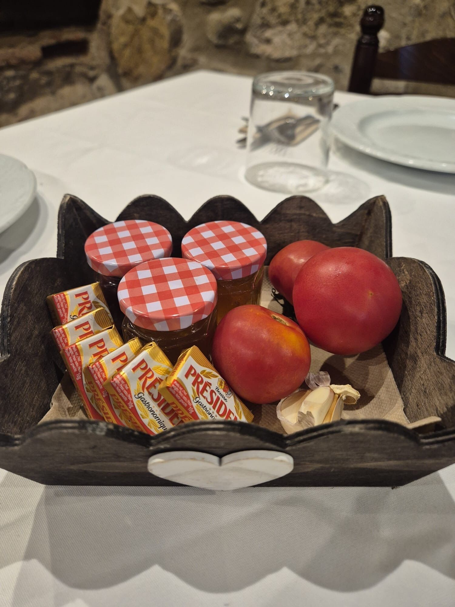 Una cesta de madera con fruta, que contiene manzanas, miel y frascos de conservas sobre una mesa.