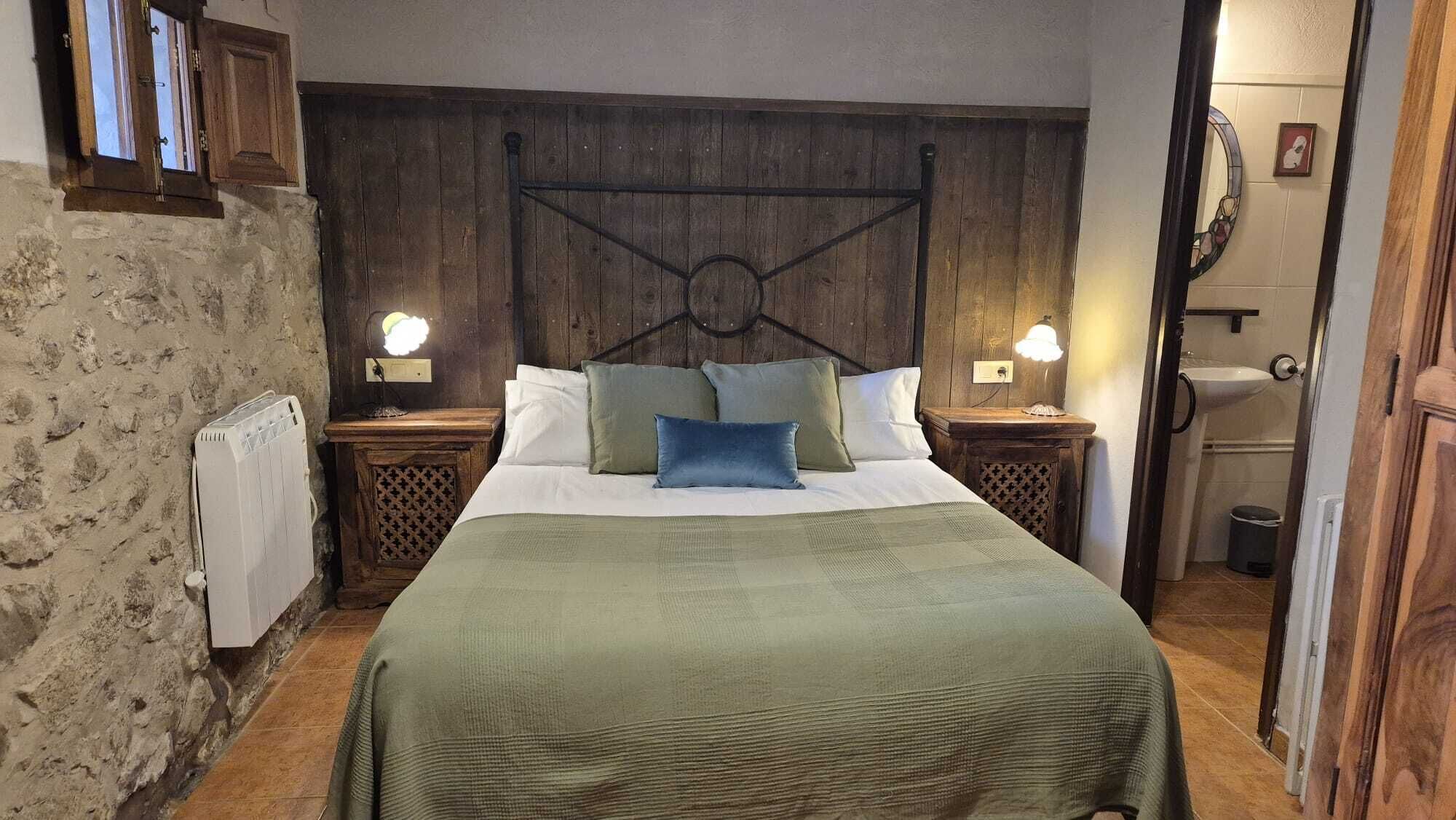 A bedroom with a wooden headboard, a bed with green bedding, two bedside lamps, and a small bedside table.