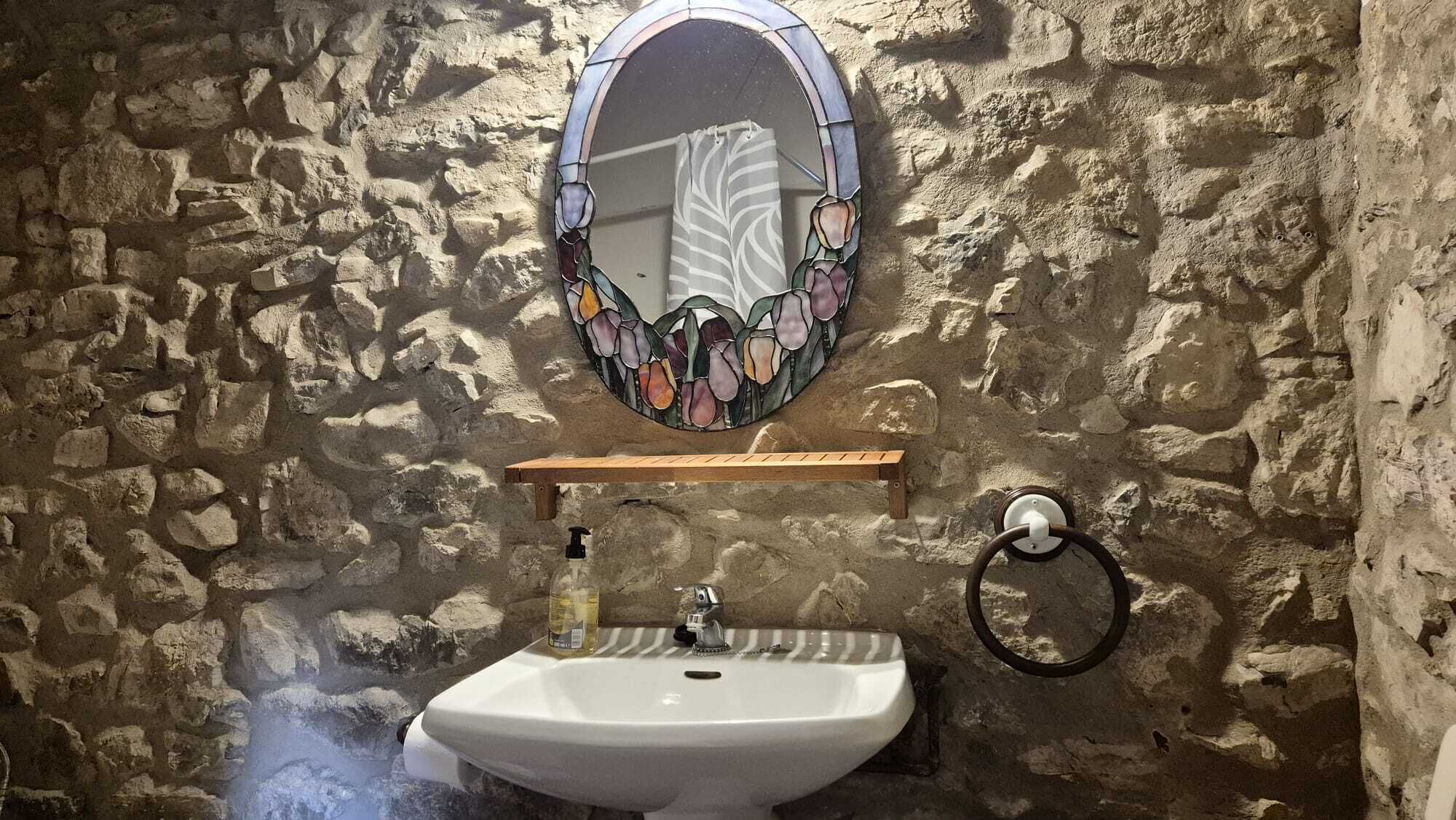 A bathroom with a stone wall, a white sink, a mirror with a stained glass design, and a towel rack.