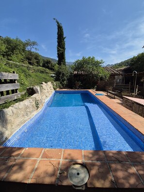 A rectangular swimming pool with blue mosaic tiles, surrounded by stone walls and wooden benches.