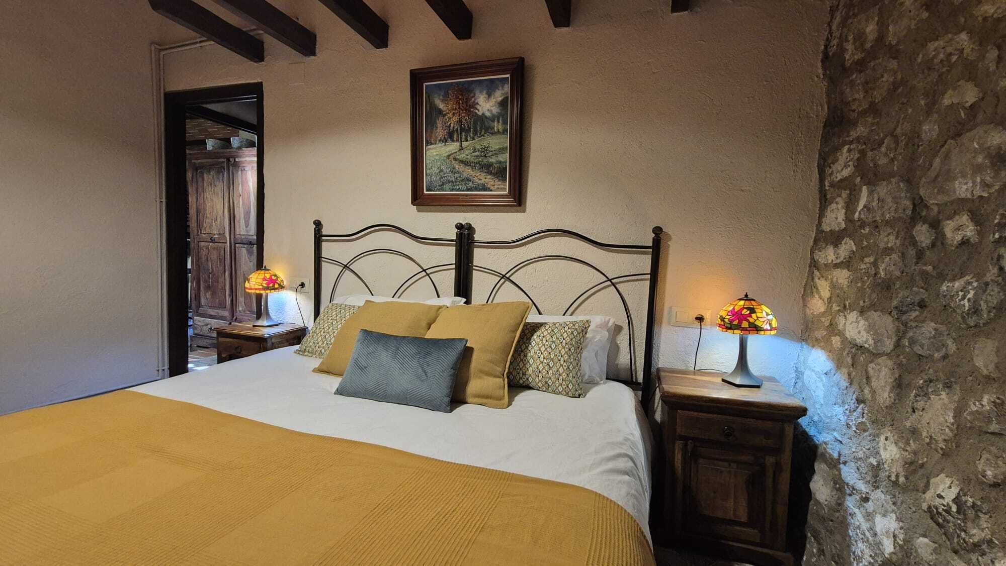 Une chambre à coucher avec un lit, deux tables de chevet, un tableau au mur et un mur en pierre.