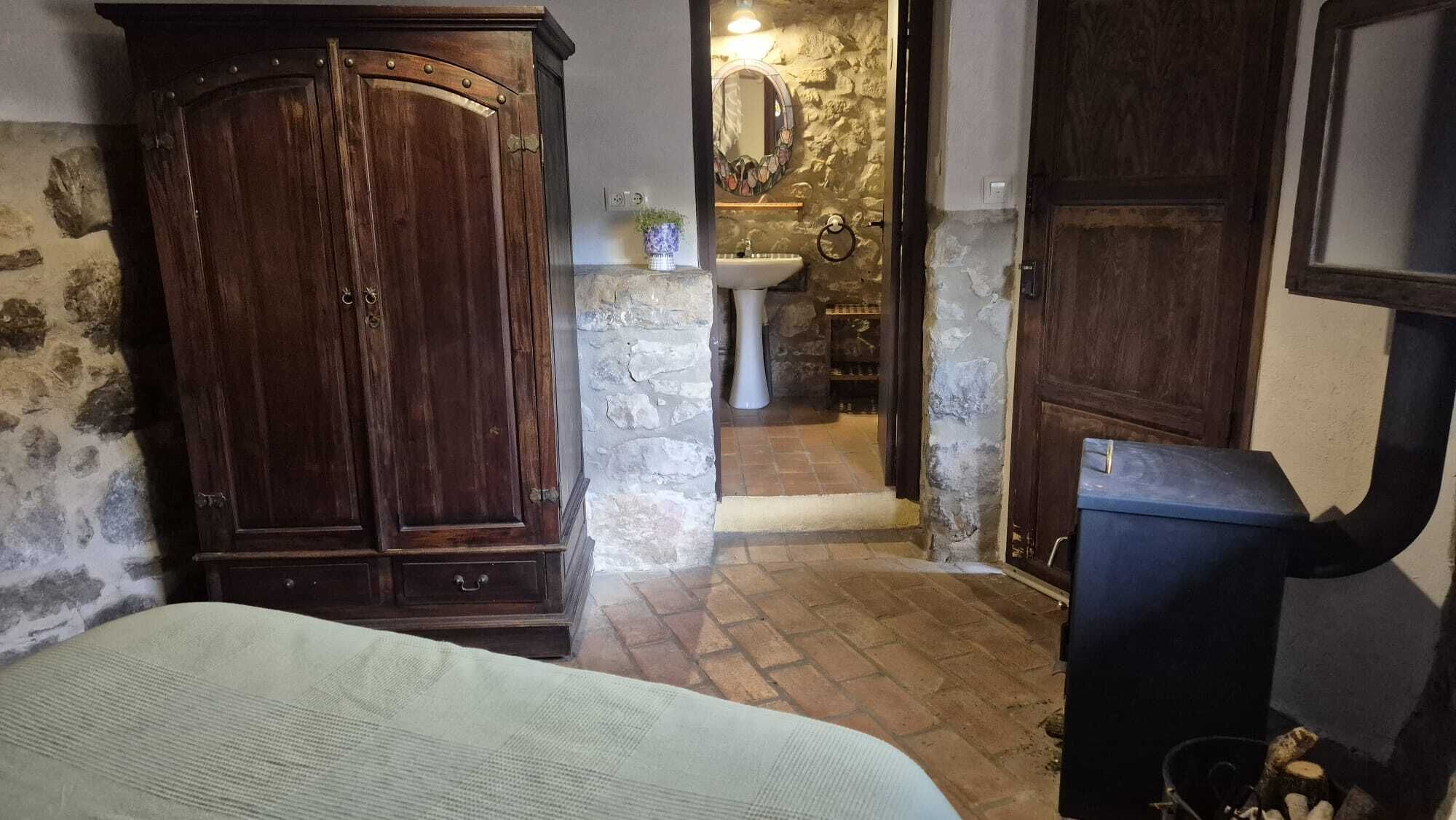 Ein Zimmer mit einem Bett, einem Holzschrank, einer Steinwand, einem Waschbecken und einem Spiegel.
