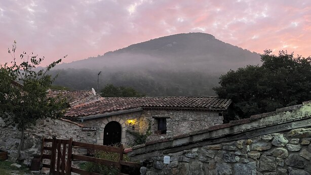 A rustic stone building with a tiled roof, a wooden gate, and a stone wall.
