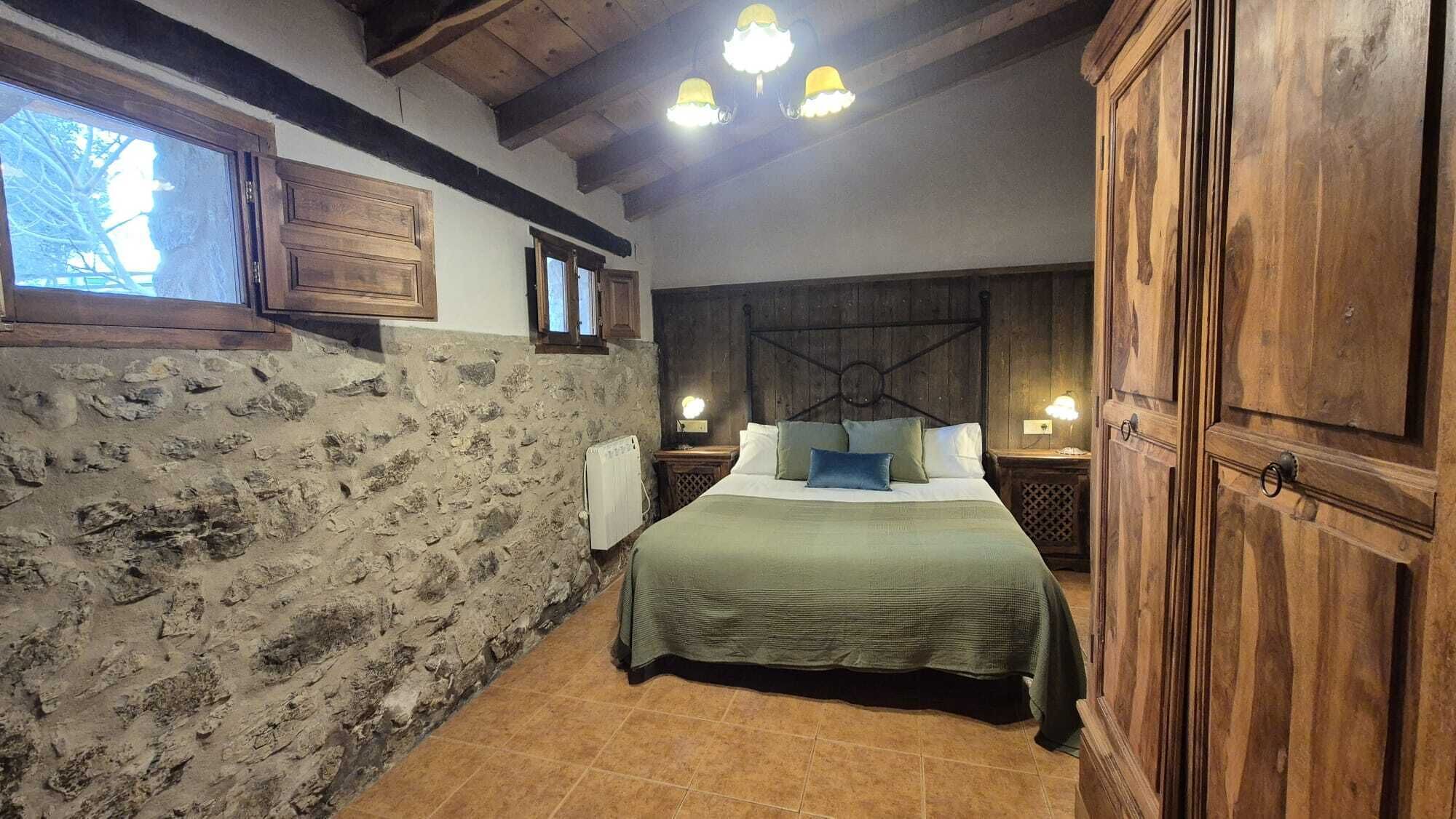 Un dormitorio rústico con pared de piedra, cabecera de madera y un gran armario.