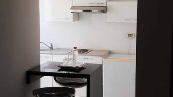 A modern kitchen with white cabinets, a stainless steel range hood, and a black countertop with a bowl and a bottle.
