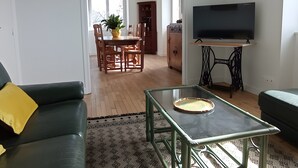 A living room with a sofa, a coffee table, a television, a dining area with chairs and a table, and a kitchen area with cabinets. - Fully Renovated Cottage in Basse Corrèze, Sleeps 8, Quiet and Scenic (Beynat)