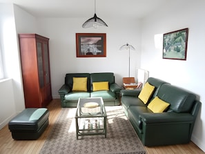 Ein Wohnzimmer mit einem grünen Sofa, einem kleinen Tisch, einem Schrank und zwei Pendelleuchten.