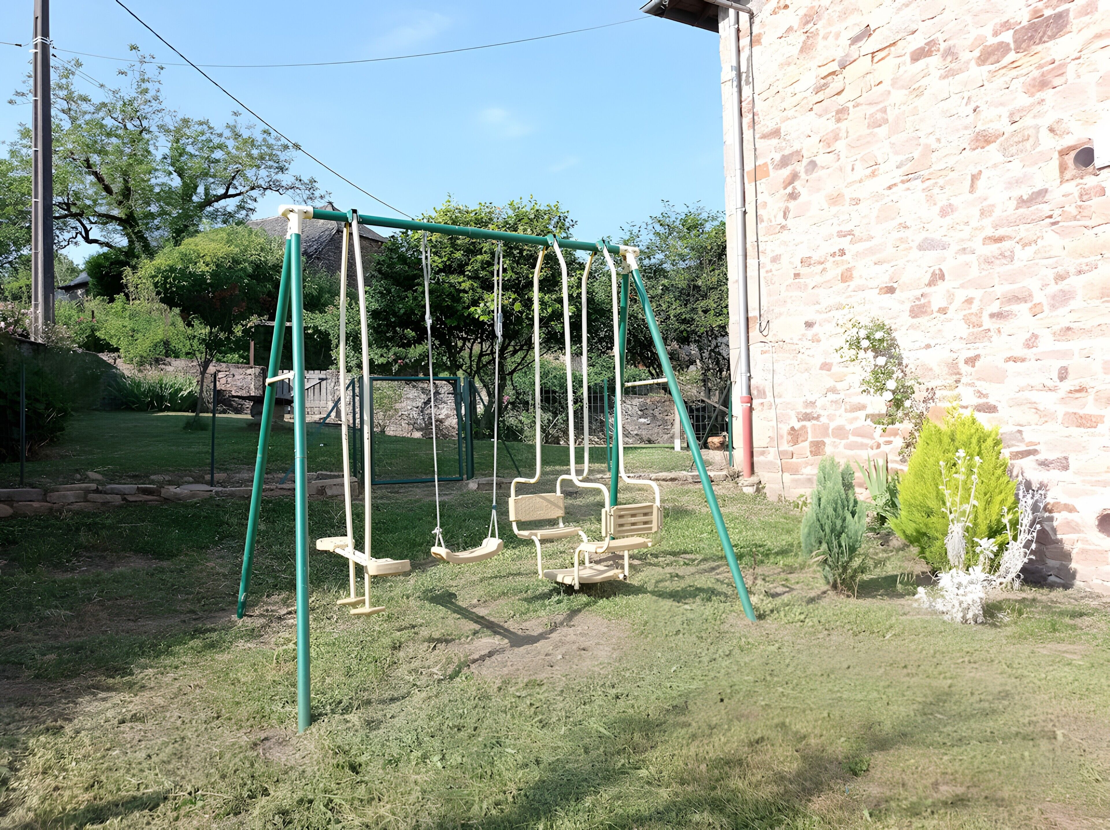 Une balançoire installée dans une cour verdoyante, avec un bâtiment en pierre en arrière-plan.