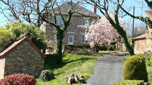 A stone house with a paved driveway, surrounded by lush greenery and flowering bushes. - Fully Renovated Cottage in Basse Corrèze, Sleeps 8, Quiet and Scenic (Beynat)
