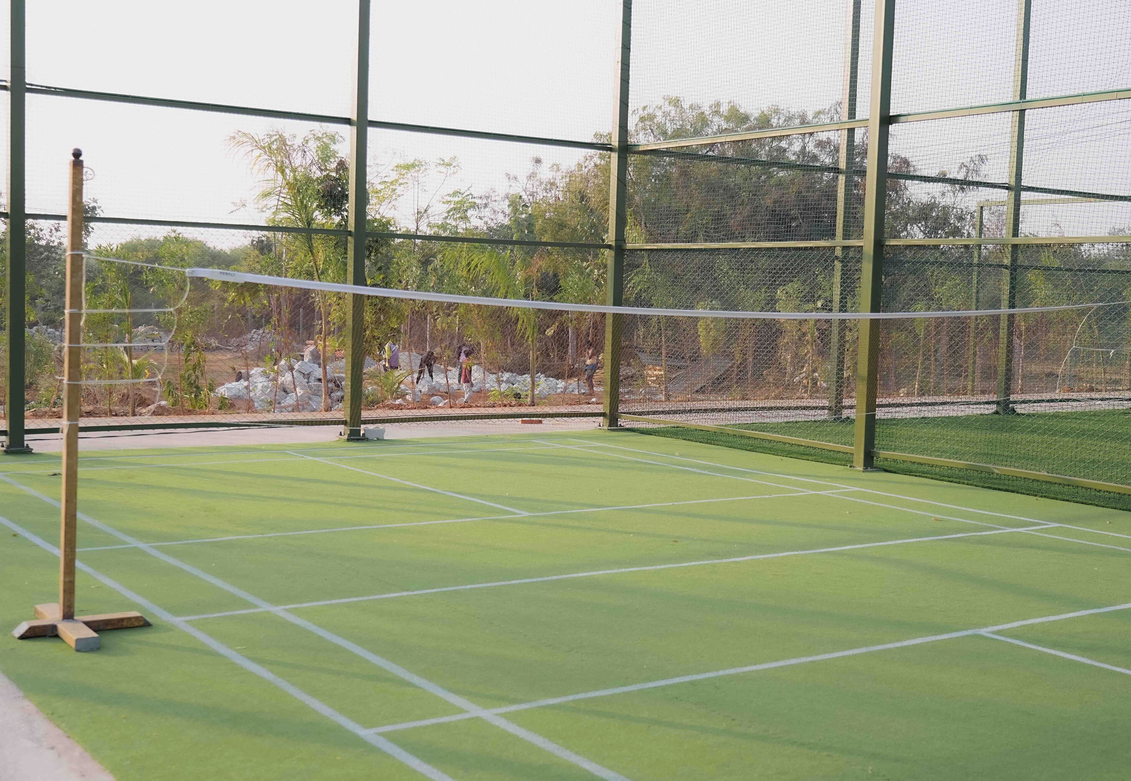 A tennis court with a net, surrounded by a fence and trees.