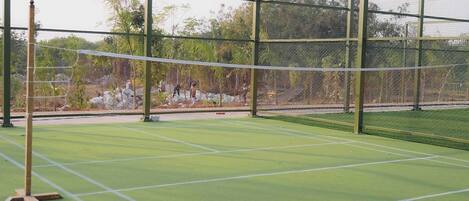 A tennis court with a net, surrounded by a fence and trees.