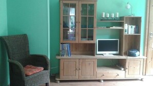 A room with a green wall, a wicker chair, a wooden cabinet with a television, and a bookshelf.