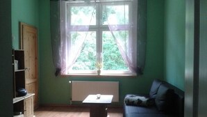 A room with a window, a radiator, a table, a sofa, and a wooden cabinet.