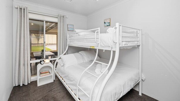 Une chambre avec un lit superposé blanc, une fenêtre, une petite table de chevet et une vue sur l’extérieur.