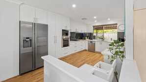 Une cuisine moderne avec des meubles blancs, des appareils électroménagers en acier inoxydable et un plancher en bois.