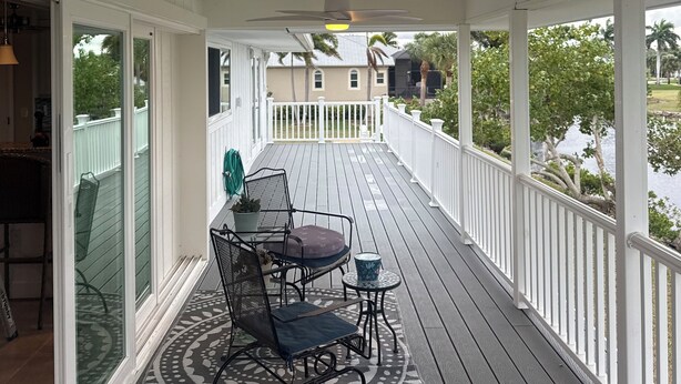 Ein überdachter Balkon mit Deckenventilator, Tisch und Stühlen und Blick auf einen See.