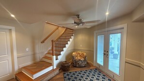 Eine Treppe mit Holzsitzen und Geländer, ein Deckenventilator, ein gemustertes Teppich und ein Sessel mit Leopardenmuster-Kissen.
