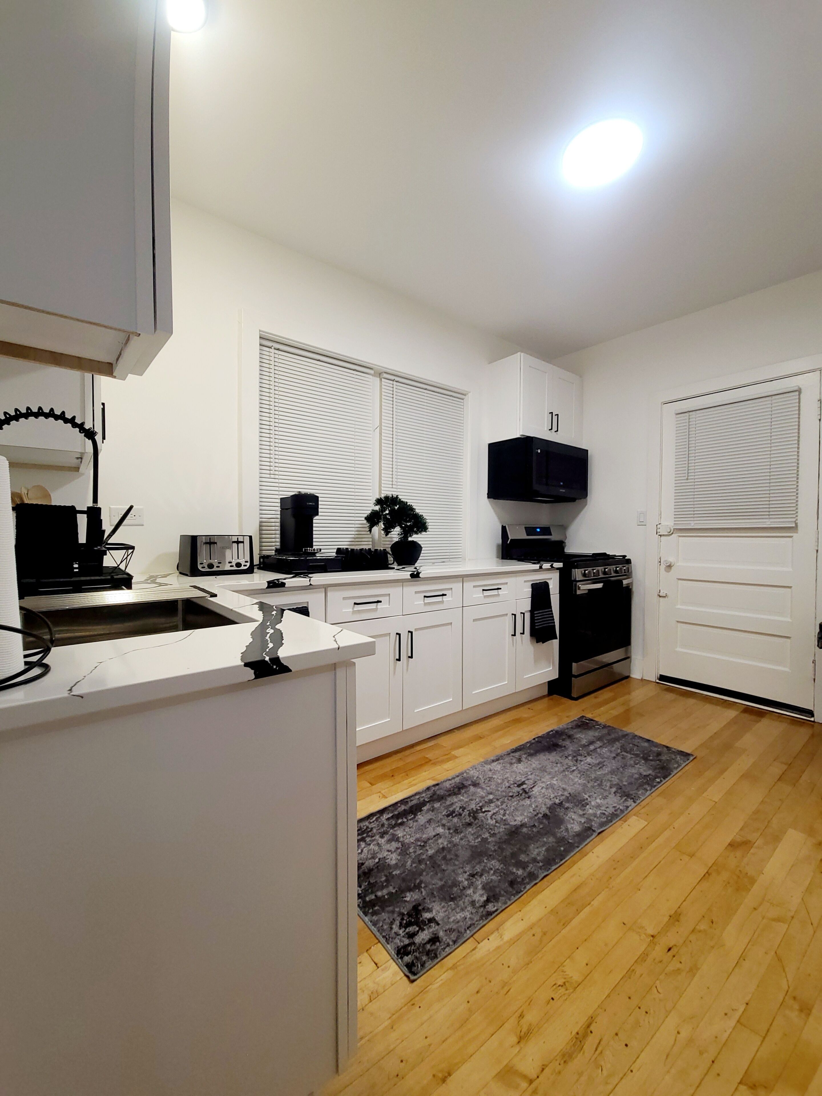 A modern kitchen with white cabinets, a built-in oven, a microwave, and a sink.
