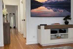 A hallway with a wooden floor, a white wall, and a mounted TV displaying a mountain landscape. - A 3-bedroom, 2-bathroom residence that provides ample space and comfort. (Chicago)