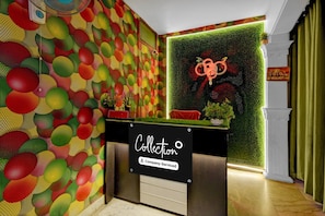 A reception desk with a colorful wall pattern, a green wall with a circular design, and a sign indicating 'Collection' and 'Company-Serviced'. - Classic Irrum Manzil Metr Green Banjara (Hyderabad)