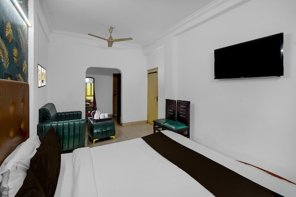 A hotel room with a bed, a desk, a chair, a television, and a ceiling fan.