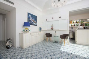 Een moderne keuken met een patroon vloer, witte kasten, een bar met flessen en een eethoek met twee stoelen.