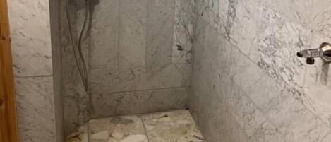 Un área de ducha pequeña y cerrada con paredes de mármol y techo inclinado.