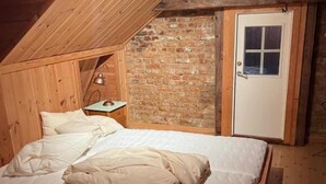 A wooden loft bedroom with a sloped ceiling, a brick wall, and a single bed with white bedding. - Fengselet Gjestegård (Nord-Aurdal)