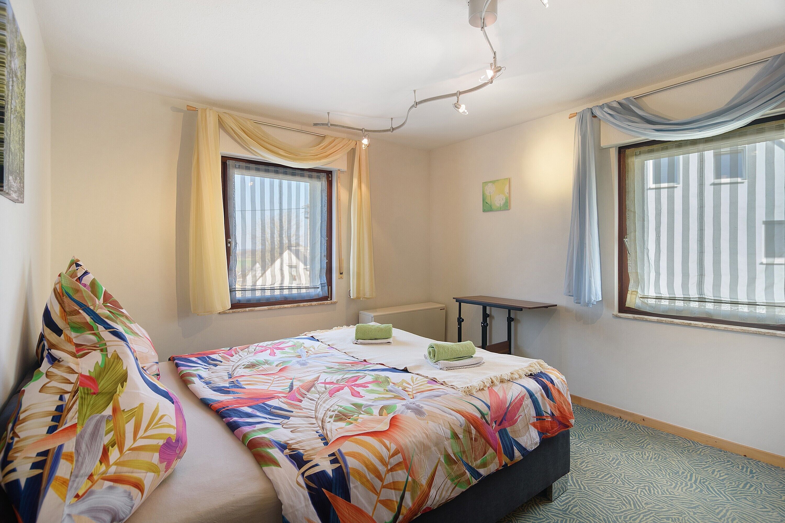 Ein Schlafzimmer mit einem Bett, zwei Kissen, einem Schreibtisch und einem Fenster mit Vorhängen.