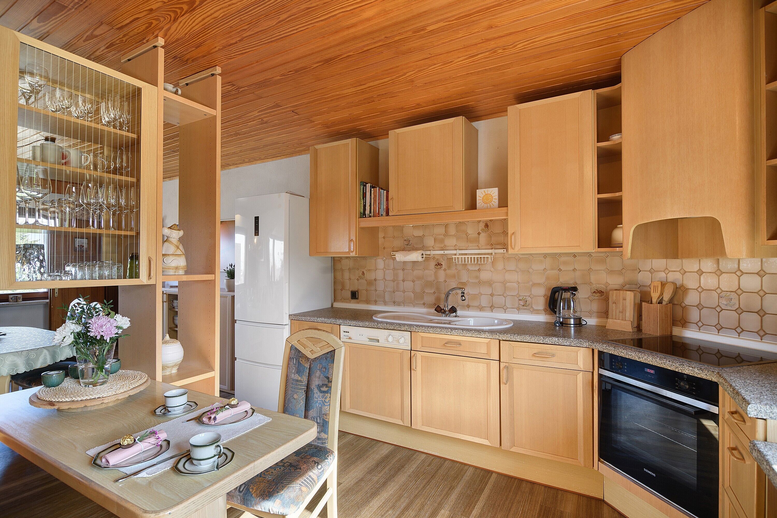Una cocina con armarios de madera, un lavamanos, lavavajillas y una zona de comedor con una mesa dispuesta para dos.