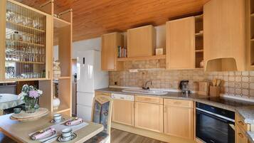 Una cocina con armarios de madera, un lavamanos, lavavajillas y una zona de comedor con una mesa dispuesta para dos.