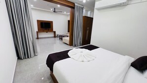 Hotellihuone, jossa on sänky, televisio, vaatekaappi sekä oleskelualue, jossa on sohva ja pöytä.