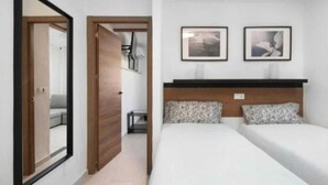 Een hotelkamer met een bed, een spiegel, een deur en twee ingelijste foto’s aan de muur.