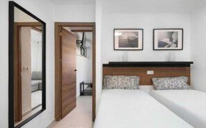 Une chambre d’hôtel avec un lit, un miroir, une porte et deux tableaux encadrés accrochés au mur.