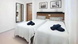 Een hotelkamer met twee bedden, witte beddengoed, een houten hoofdeinde en twee ingelijste foto's aan de muur.