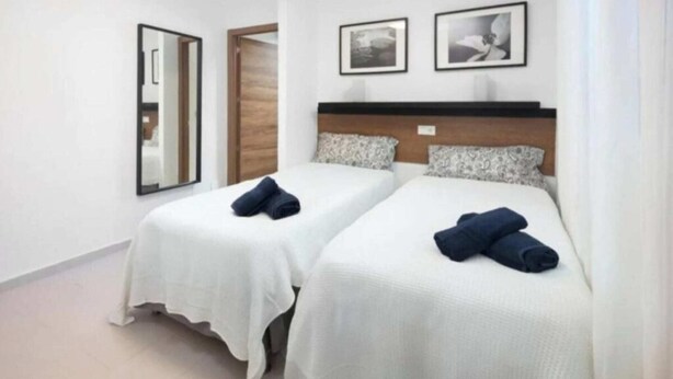 Een hotelkamer met twee bedden, witte beddengoed, een houten hoofdeinde en twee ingelijste foto's aan de muur.